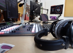 Studioatmosphäre: Blick an Kopfhörern vorbei über ein Mischpult zu Monitoren und Mikrofonen