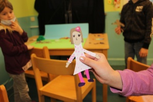 Eine Kinderhand hält eine gezeichnete und ausgeschnittene Mädchenfigur vor die Kamera