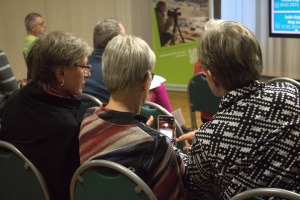 Drei Frauen hören einem Vortrag zu und schauen gemeinsam auf die Einstellungen ihres Smartphones