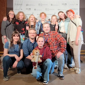 Personen der LEO-Jugendredaktion und LEO-Handpuppe posieren vor Filmkunstfest-Leinwand
